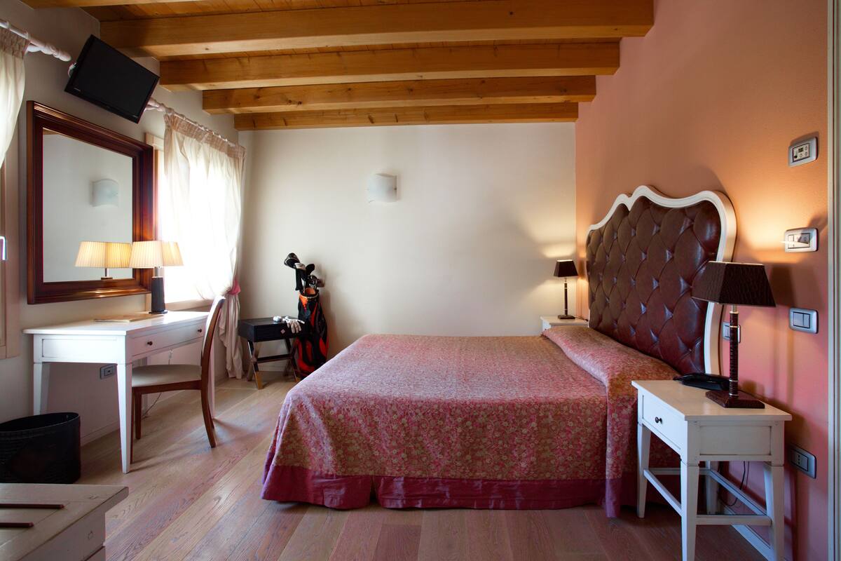 A bedroom with a bed, a desk, a chair, a television, and a lamp.