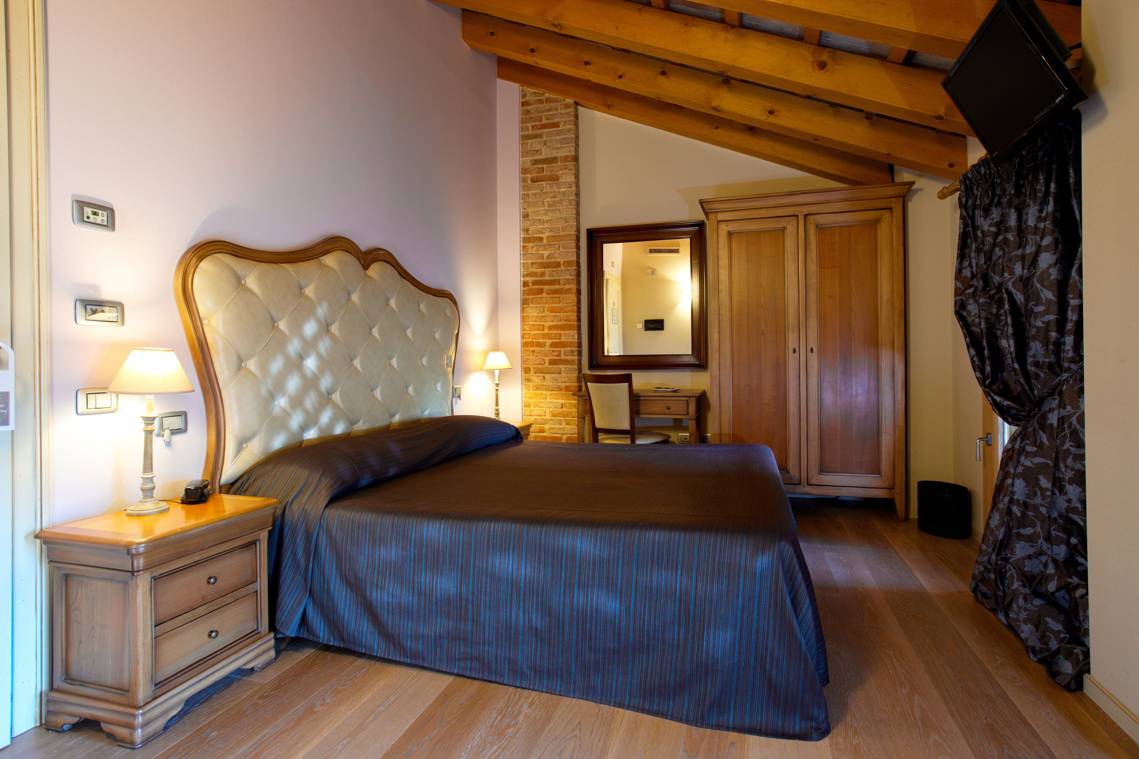A bedroom with a large bed, wooden headboard, bedside table with lamp, and a wardrobe.