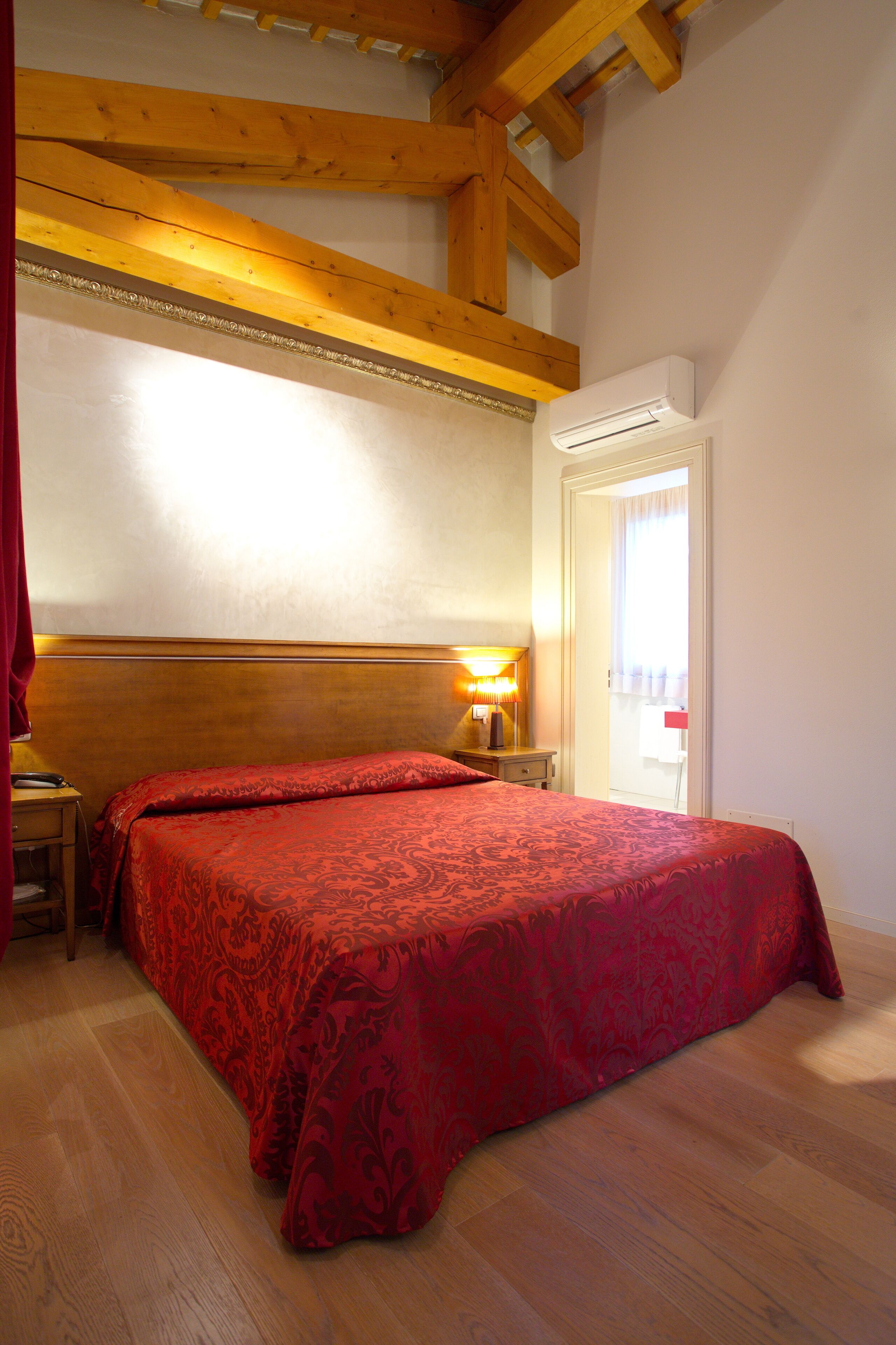 Une chambre à coucher avec une tête de lit en bois, une couvre-lit rouge, une lampe de chevet et une porte donnant sur un balcon.
