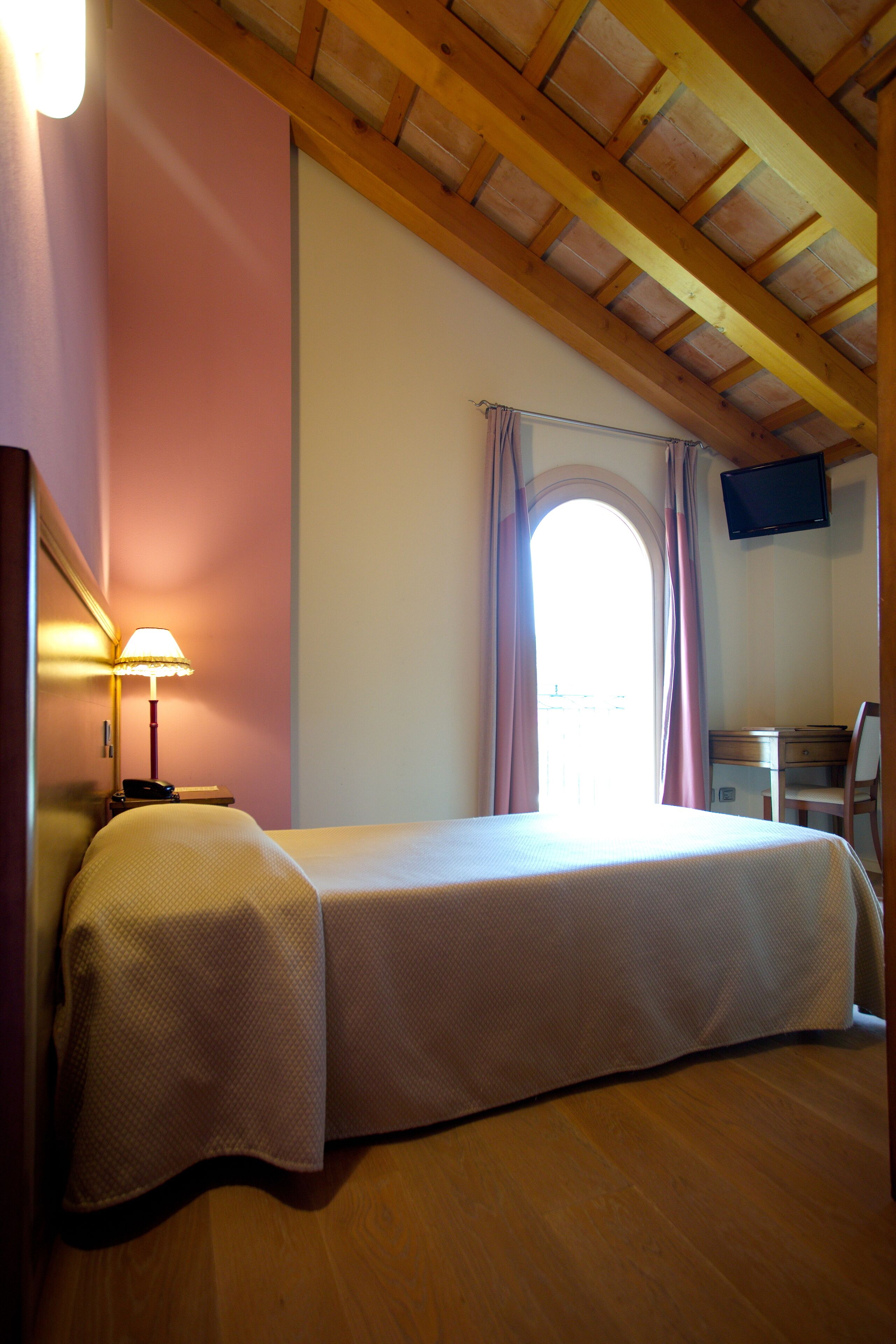 A bedroom with a bed, a desk, a chair, a TV, and a window with curtains.