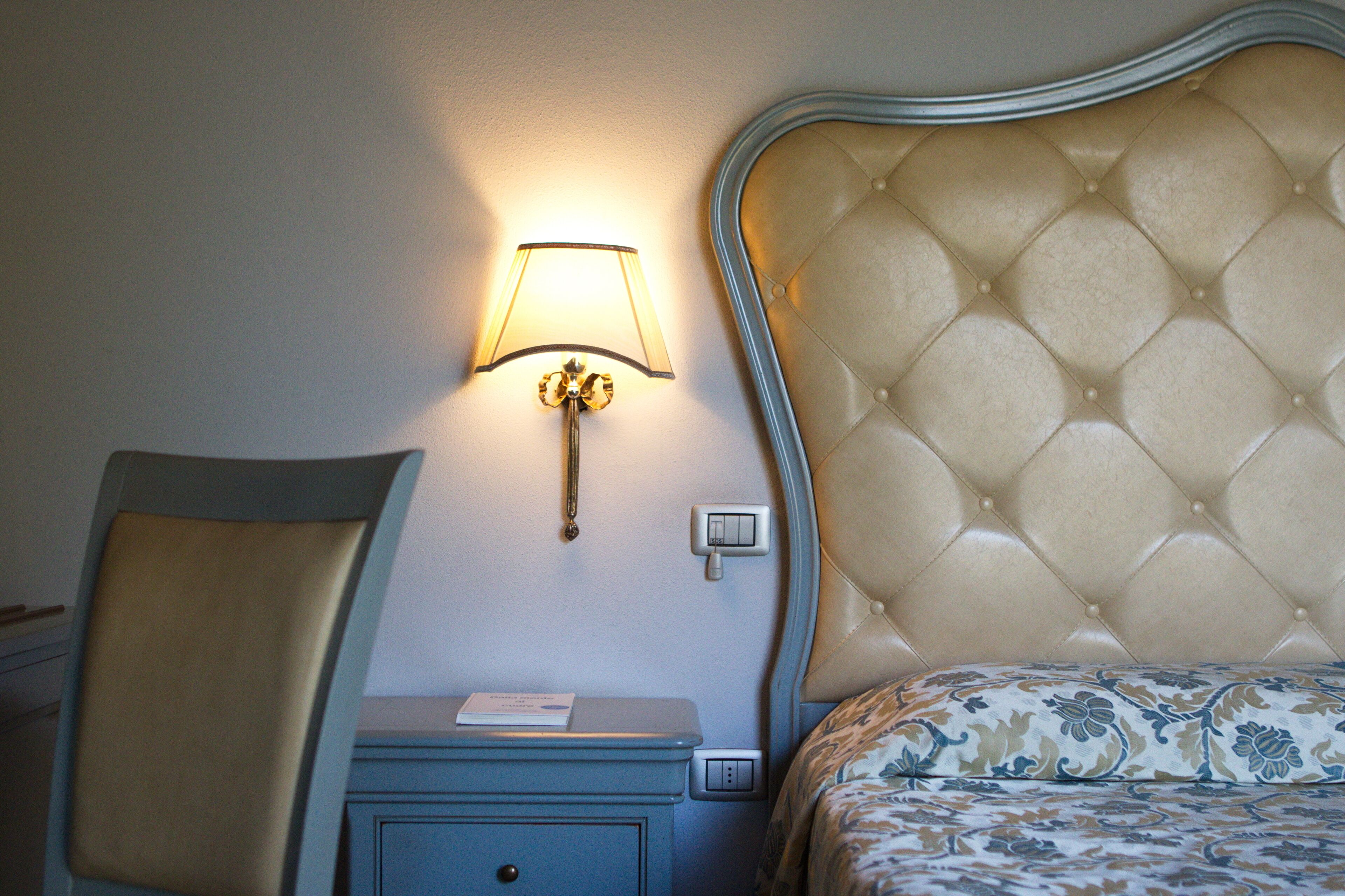 Un dormitorio con cabecera capitonada, una mesita de noche con lámpara y una silla.