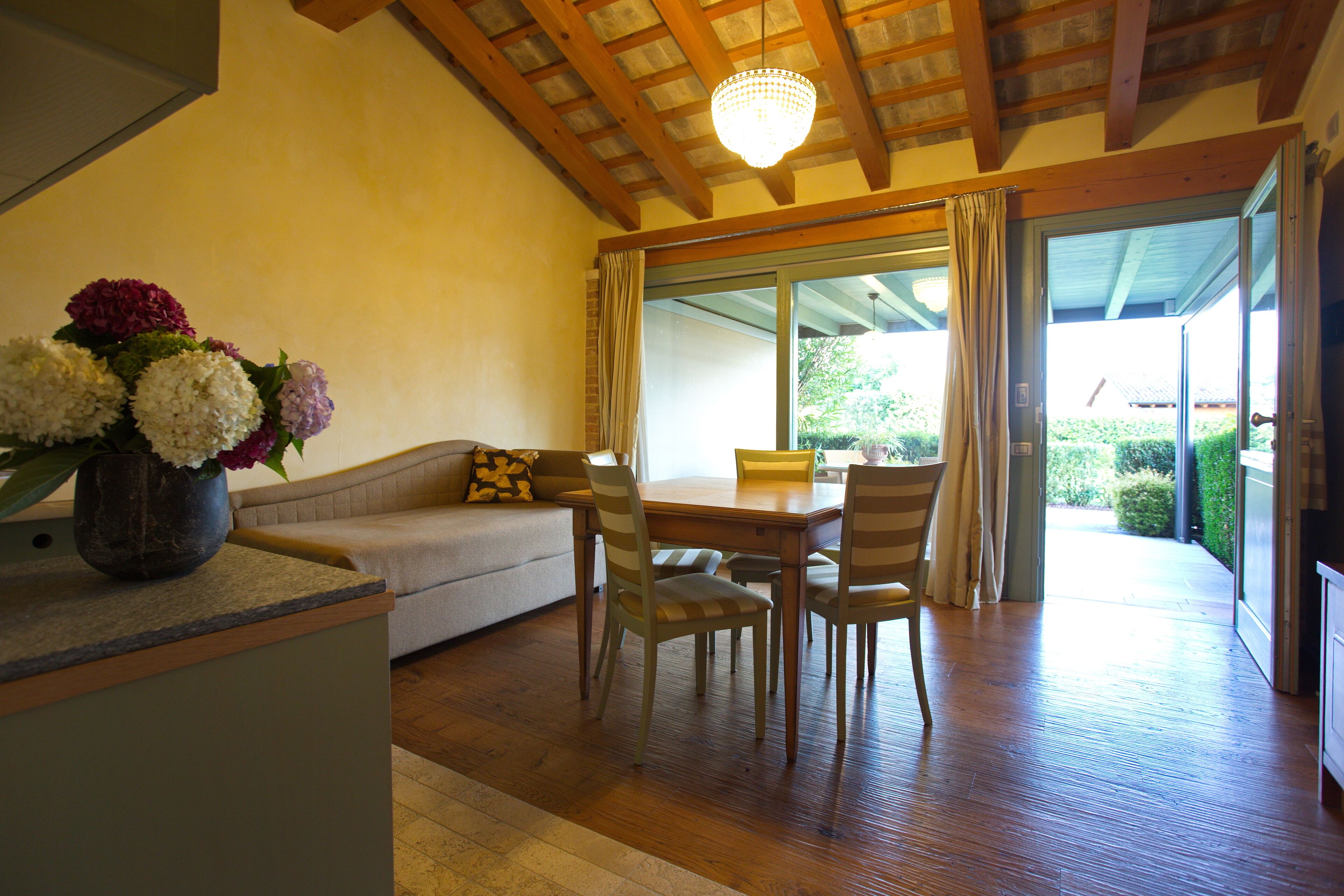 A dining area with wooden flooring, a table, chairs, and a vase of flowers.