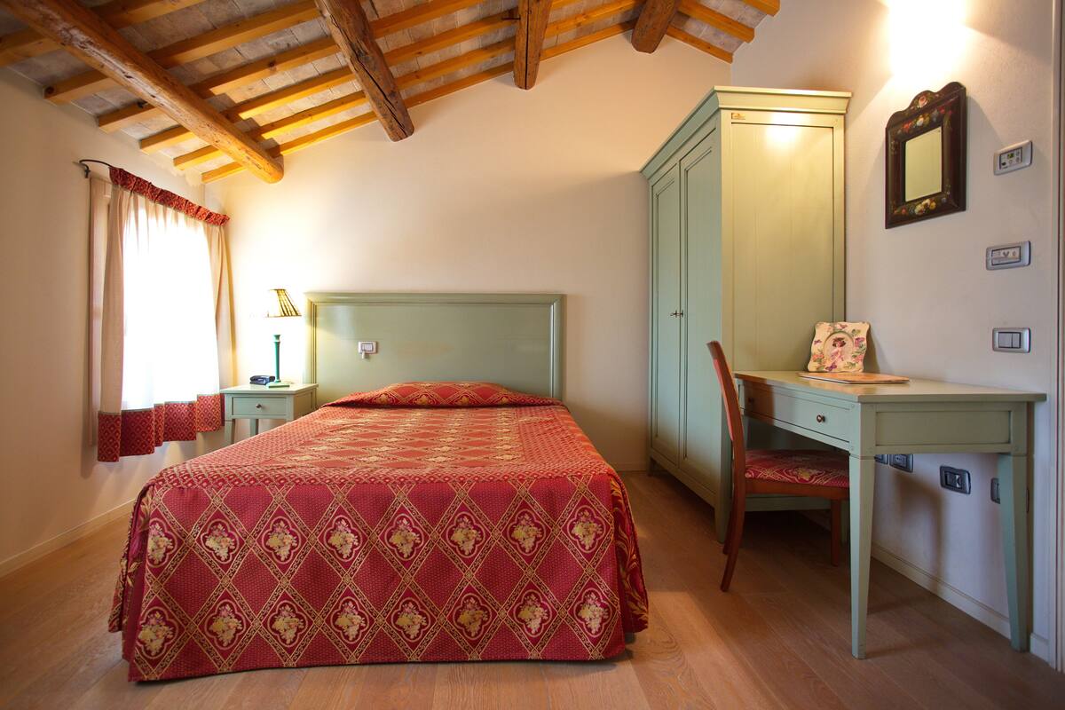 A bedroom with a bed, a desk, a chair, a wardrobe, and a mirror.