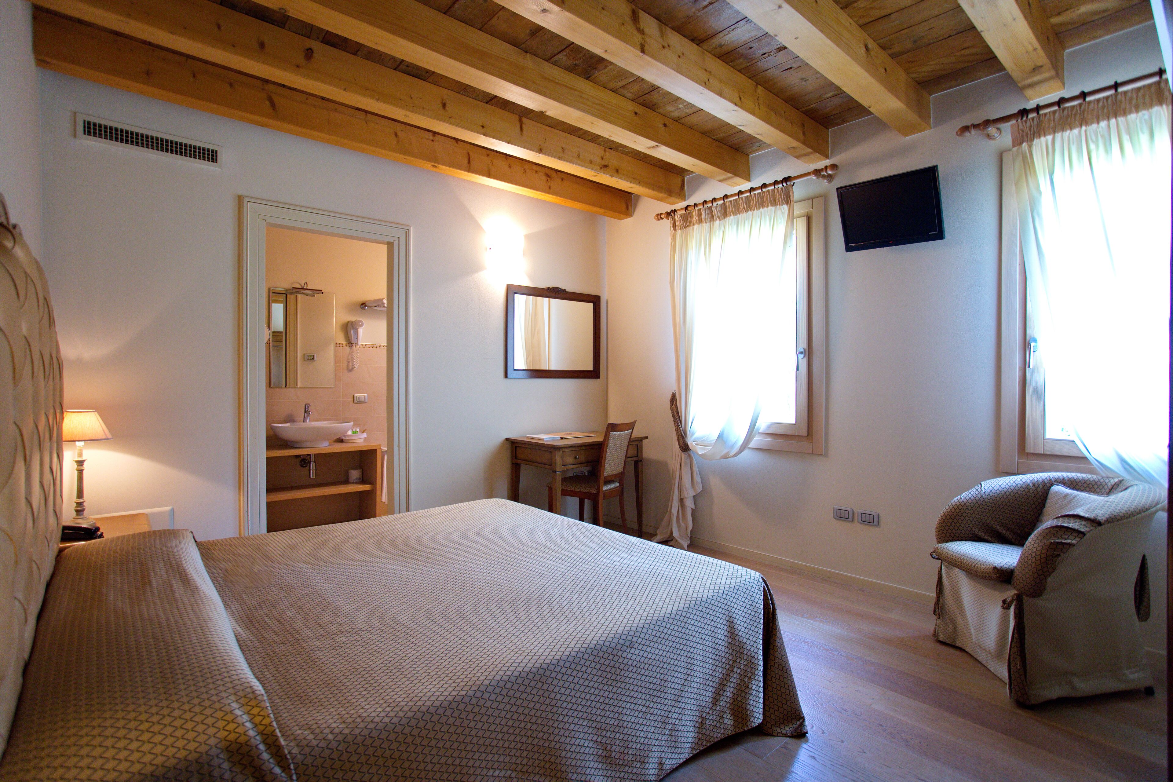A bedroom with a bed, a desk, a chair, a television, and a bathroom visible through an open door.