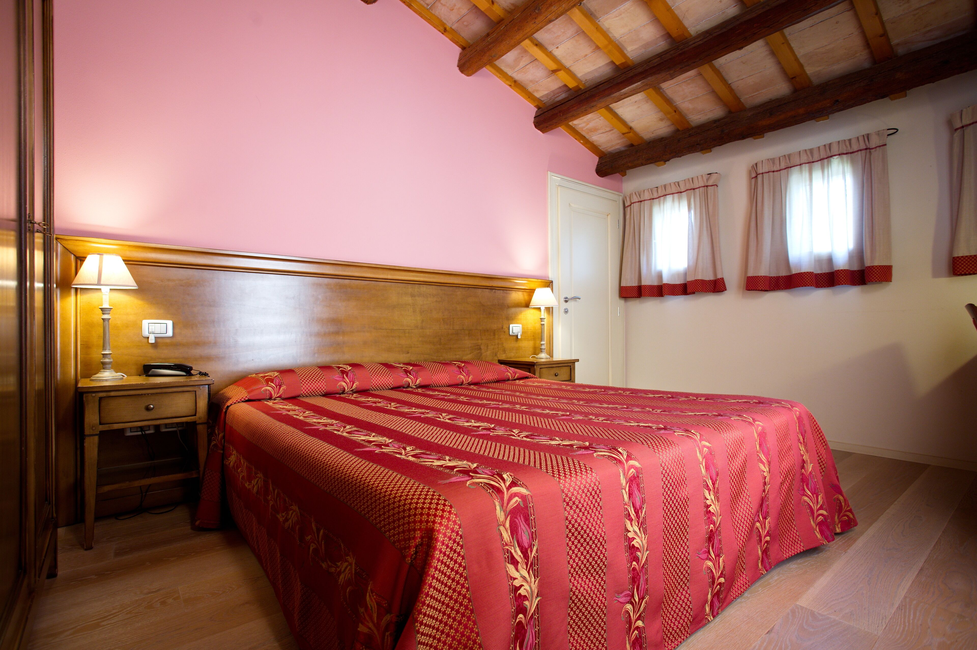 A bedroom with a wooden headboard, two bedside lamps, a telephone, and a red bedspread.