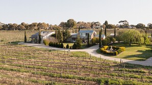 Una finca vitivinícola con una casa grande, jardines cuidados y una vista despejada del paisaje circundante.