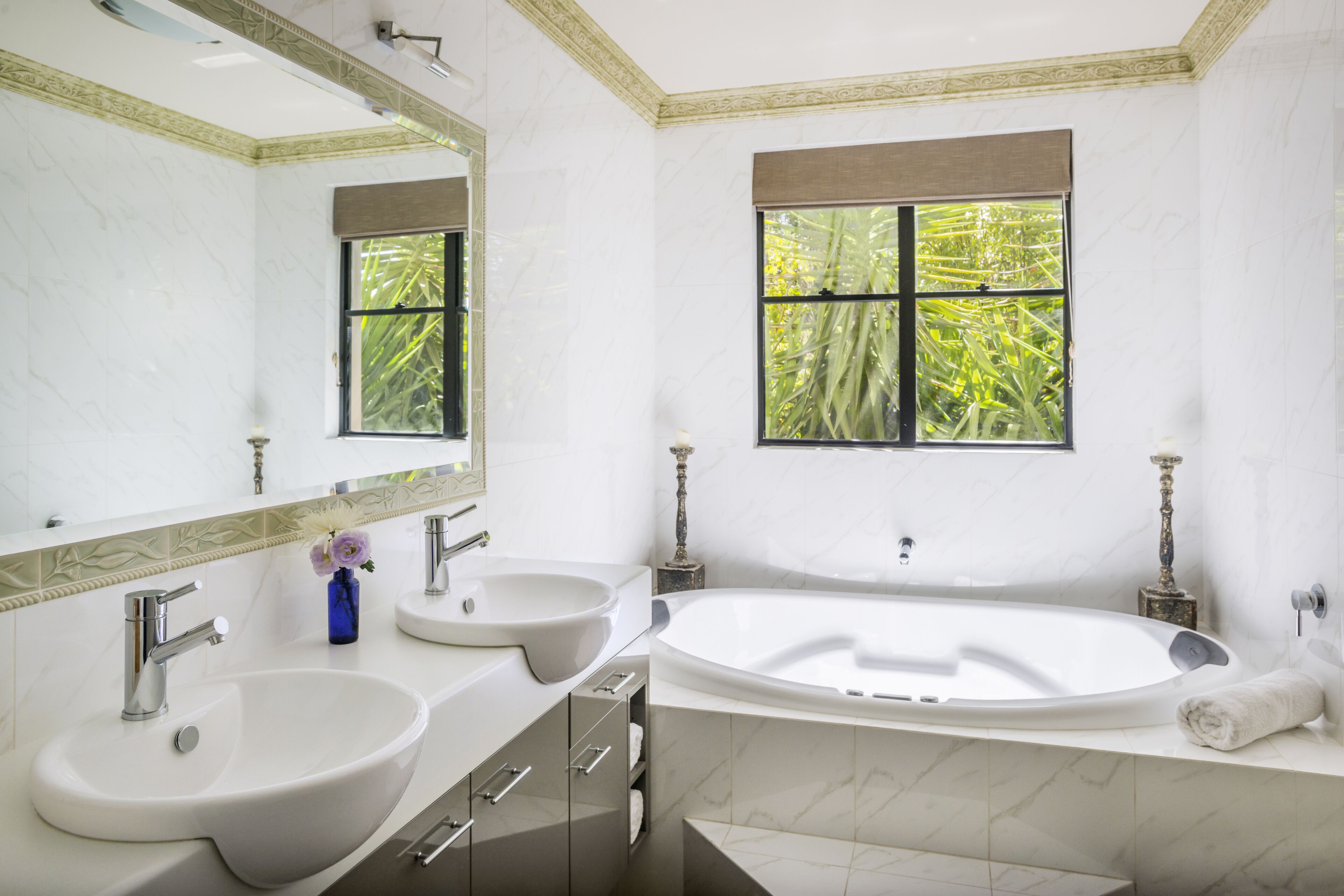 A bathroom with two sinks, a bathtub, and a window with a view of greenery.