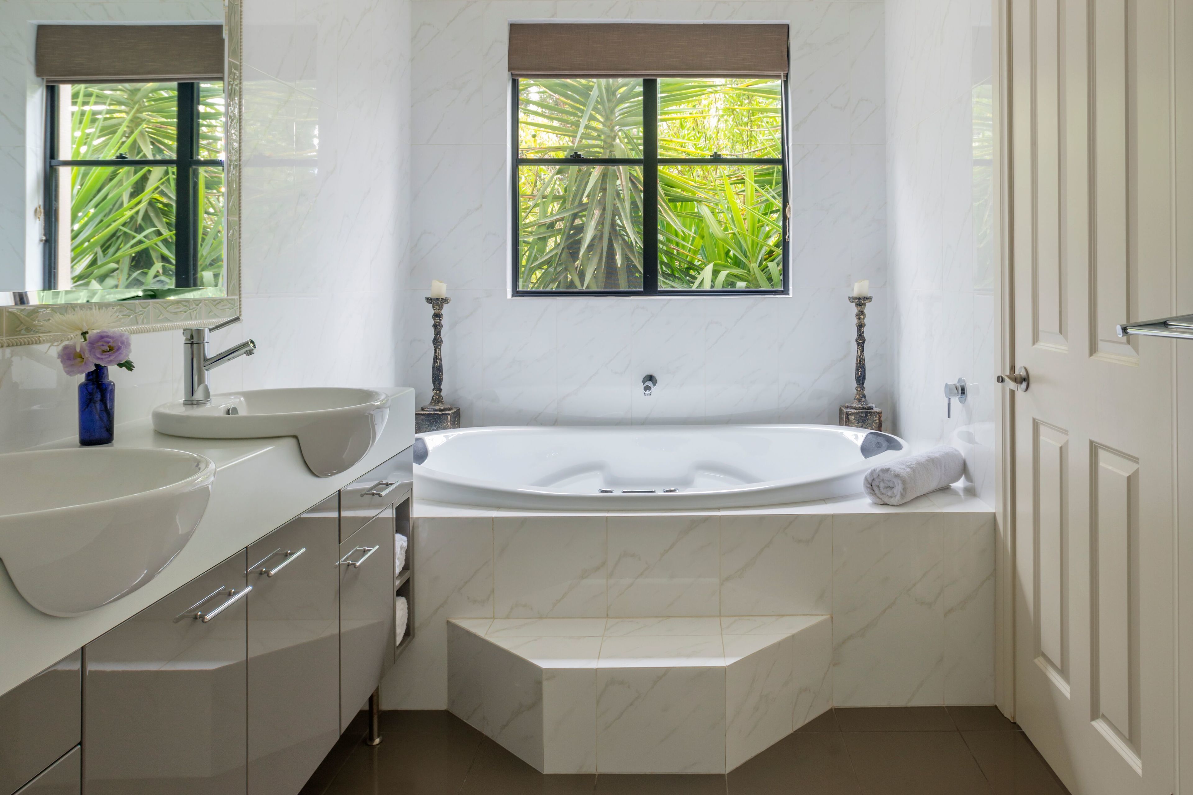 Ein modernes Badezimmer mit einer großen Badewanne, zwei Waschbecken und einem Fenster mit Blick auf Grünflächen.