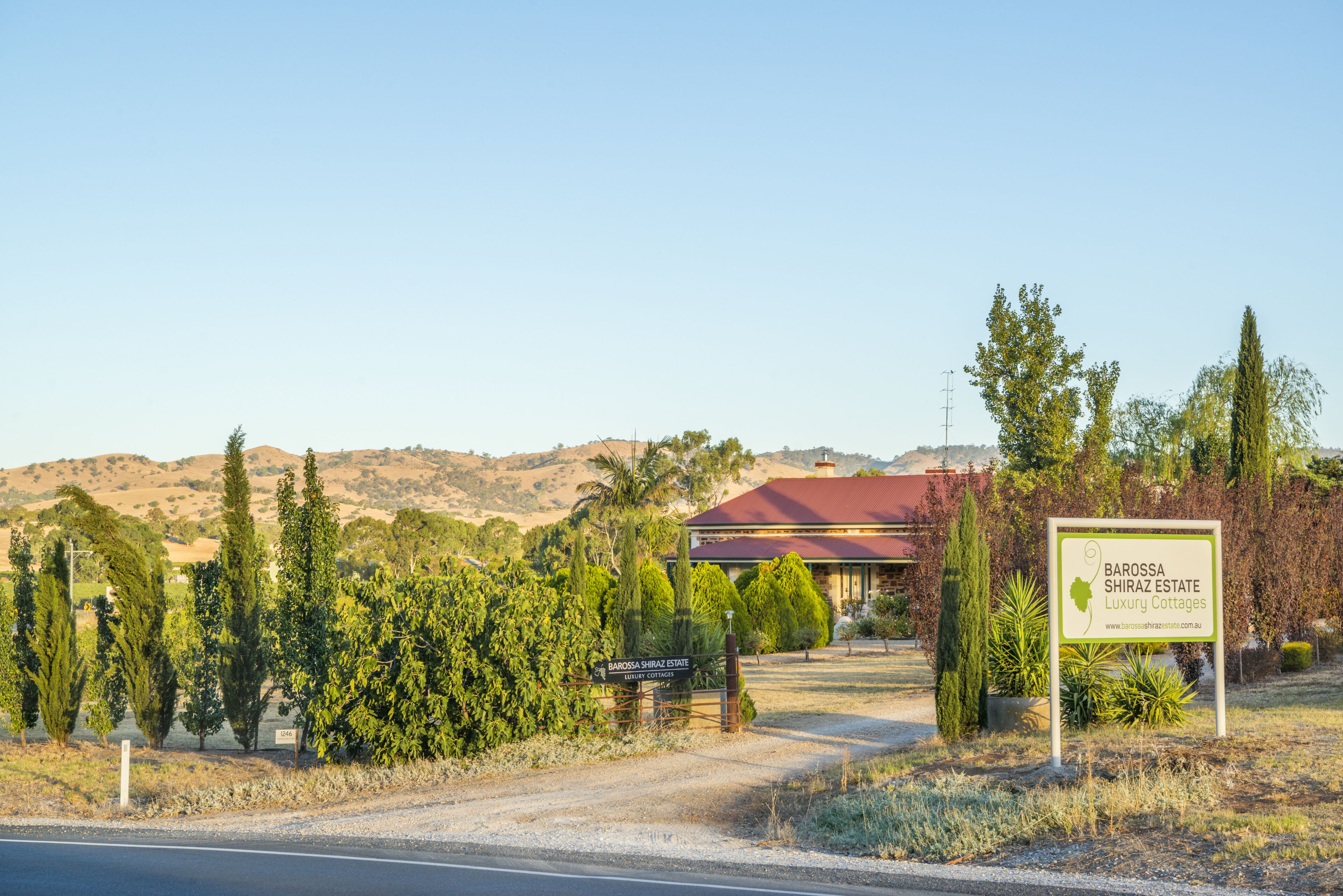 Señal de Barossa Shiraz Estate Luxury Cottages, mostrando vistas de la propiedad rodeada de árboles y colinas.
