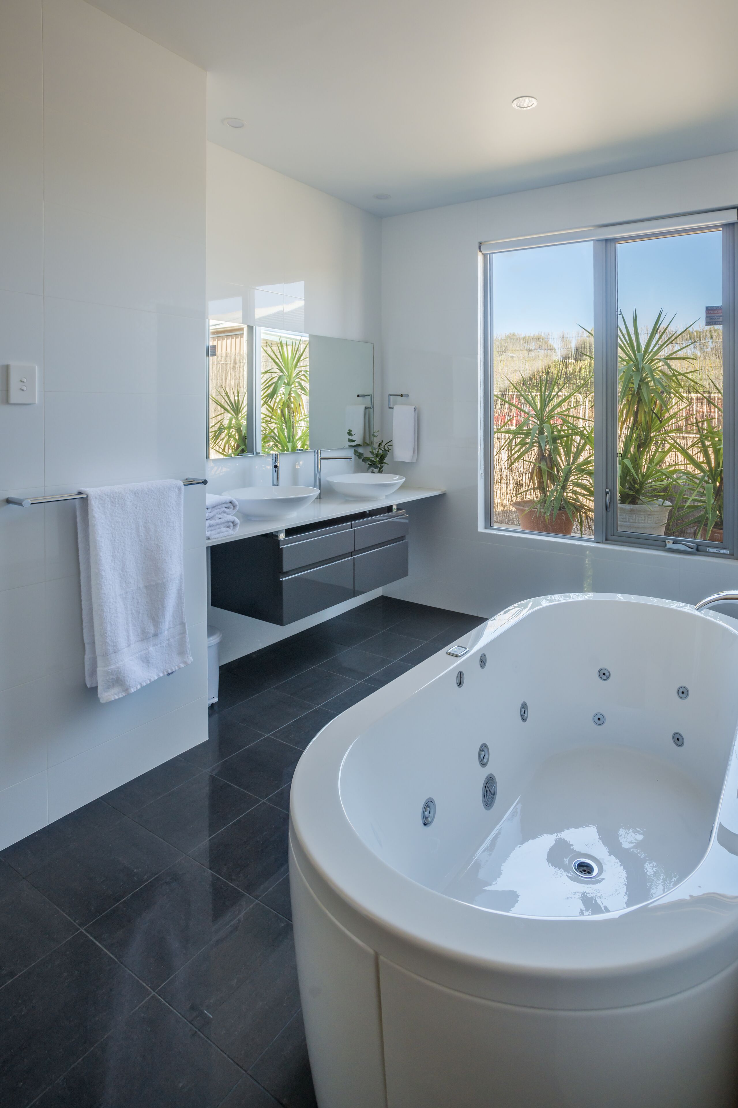 A modern bathroom with a large bathtub, a vanity with a sink, and a window with a view of palm trees.