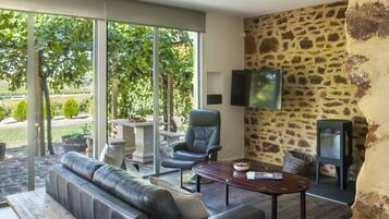 A modern living room with a stone wall, a large window, a sofa, a chair, a wooden bench, and a television.