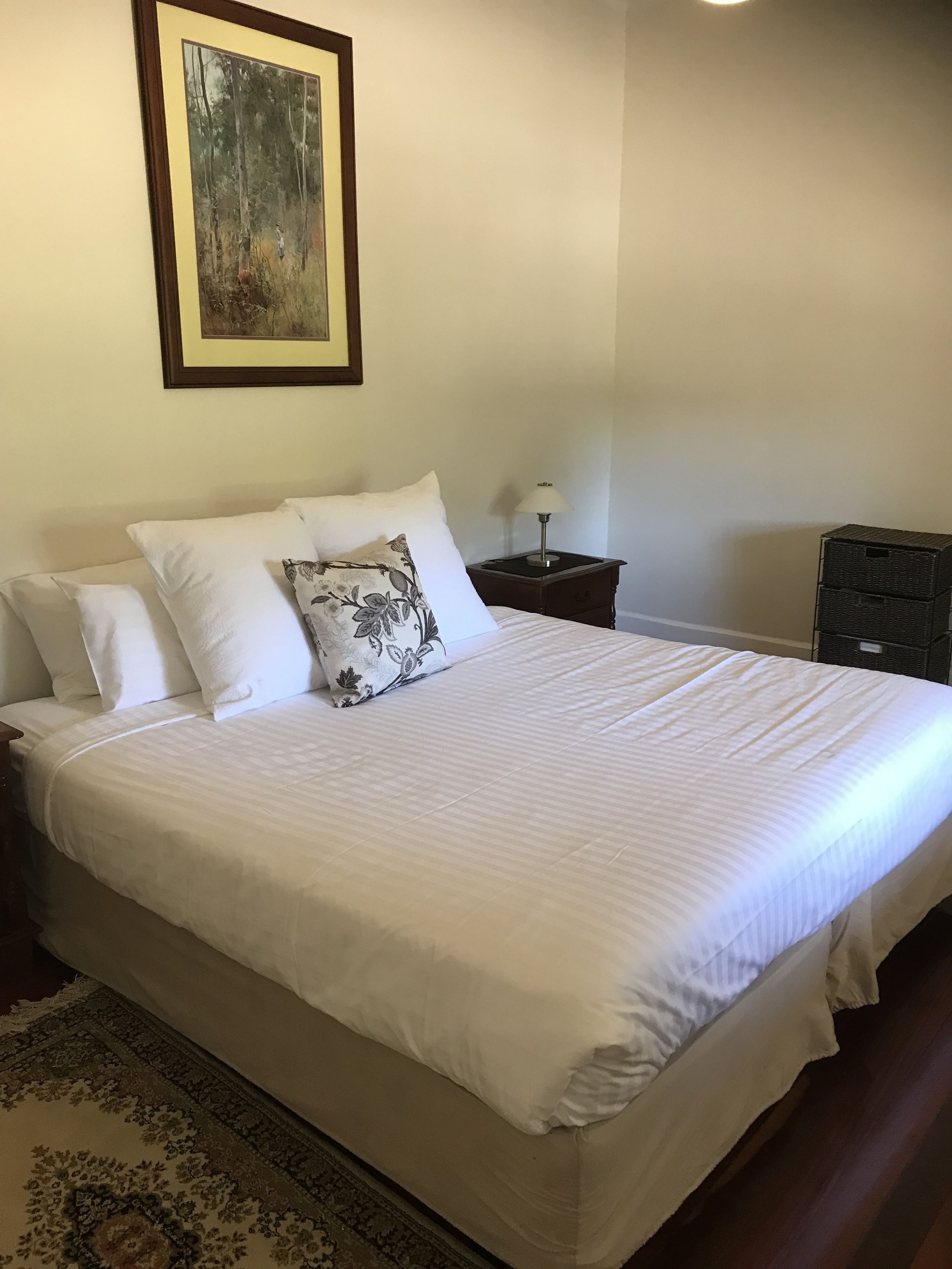 A neatly made bed with white linens, a floral pillow, and a framed artwork above it.