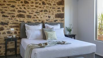 A bedroom with a stone-patterned headboard, a bed with white linens, a grey bench, and a nightstand with a vase.
