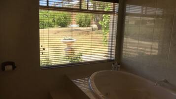 Un bagno con una vasca da bagno ampia, una finestra con persiane e vista su un giardino.
