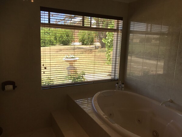 Un baño con una bañera grande, una ventana con persianas y vistas a un jardín.