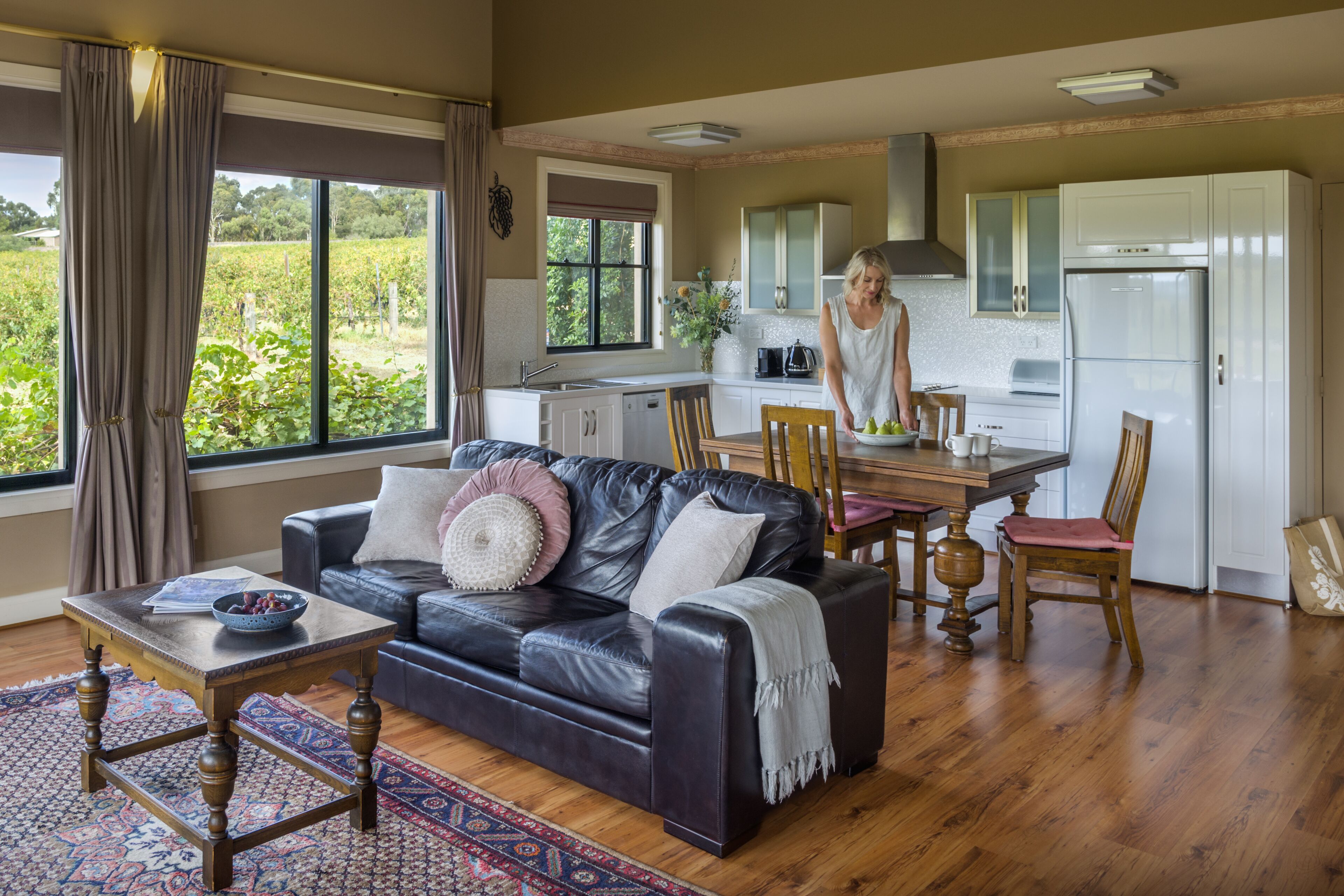 A spacious living room with a leather sofa, a dining table, and a kitchen area with white cabinets and a refrigerator.