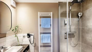 A modern bathroom with a shower, a towel rack, a hairdryer, and a plant.