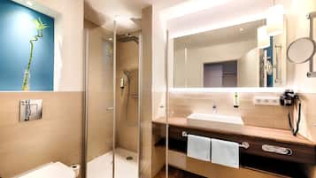 A modern bathroom with a glass-enclosed shower, a wooden vanity with a mirror, and a toilet.