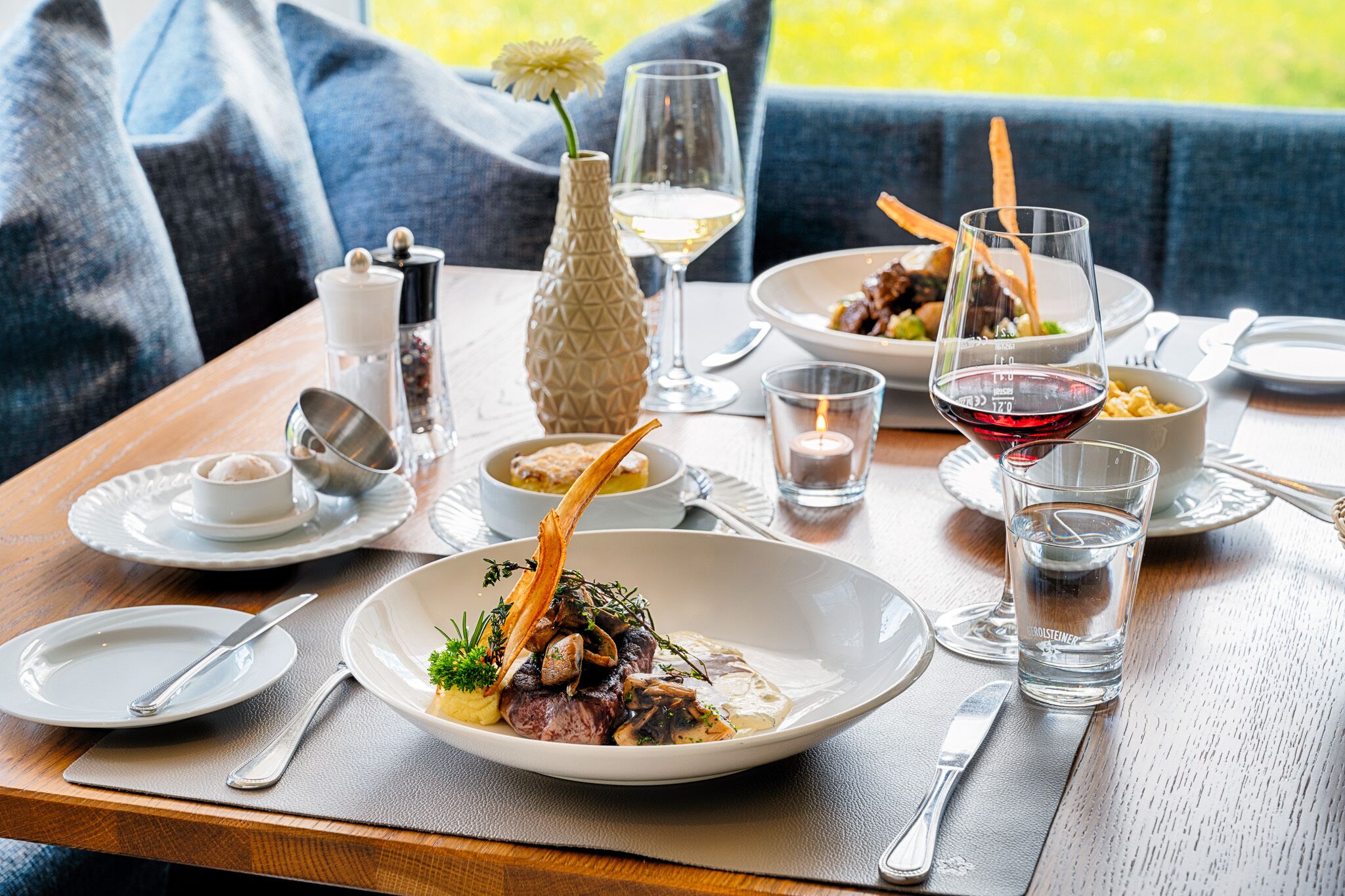 A dining table set with plates of food, glasses of wine, and a candle.