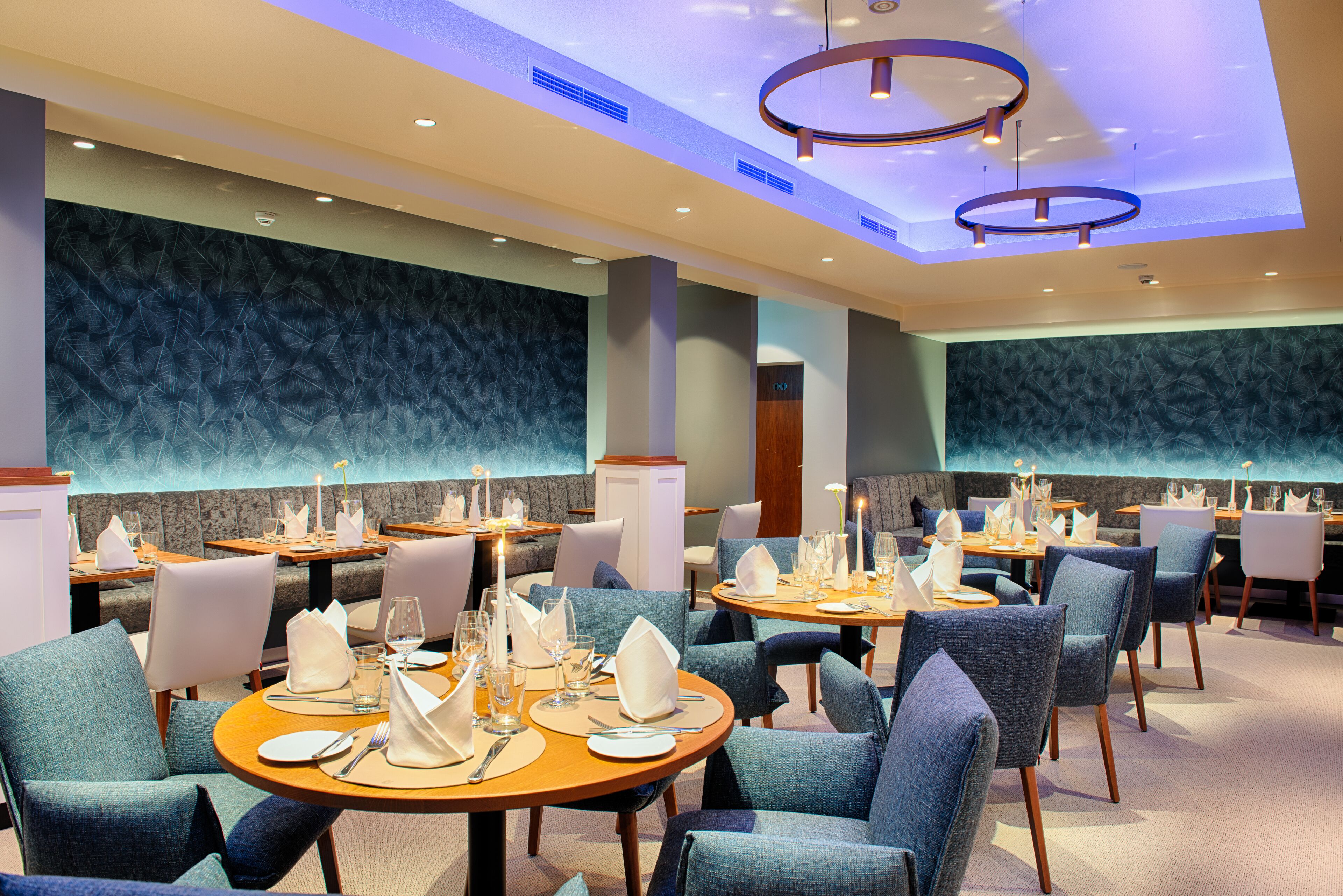 A restaurant with round tables, blue upholstered chairs, and a modern ceiling design.