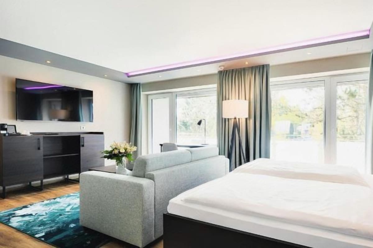 A modern hotel room with a large bed, a sofa, a TV, and a desk.