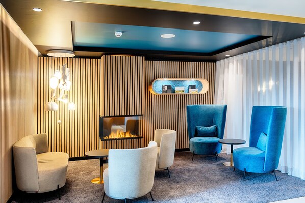 A modern lounge area with a fireplace, seating, and a decorative wall panel.