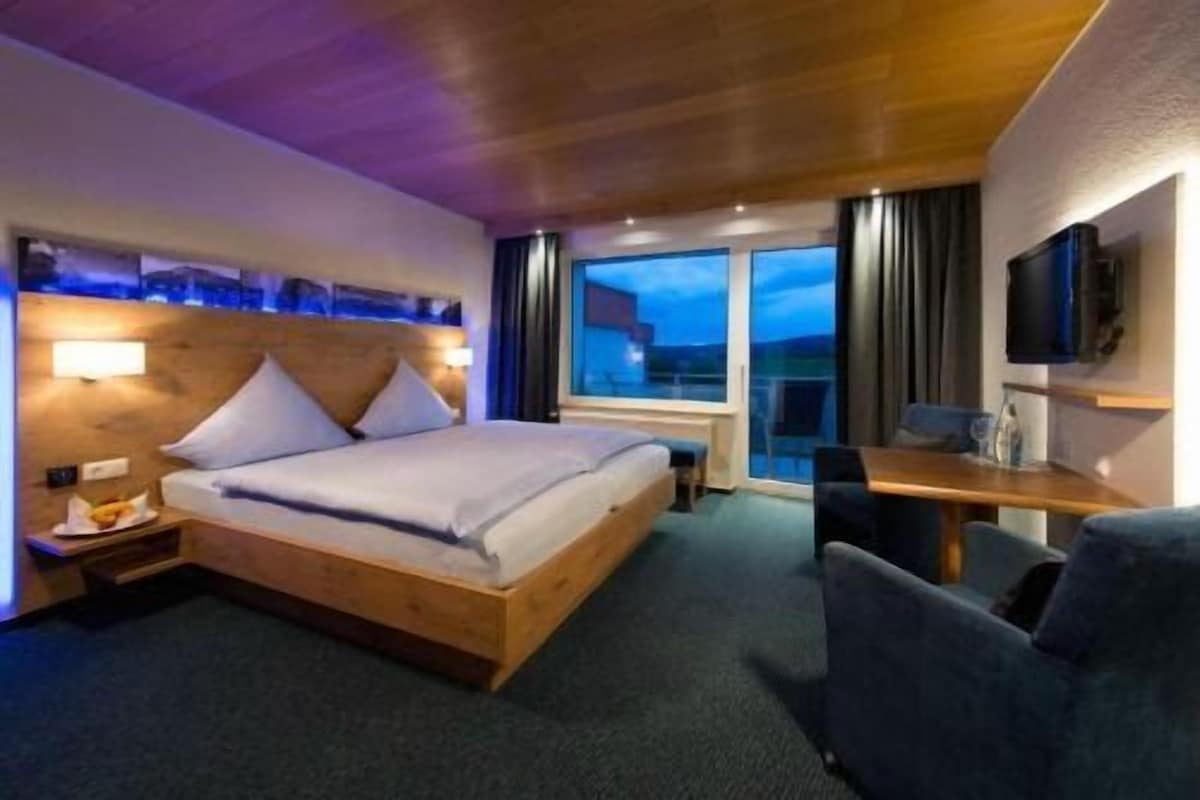 A hotel room with a bed, a desk, a chair, a TV, and a window with a view.