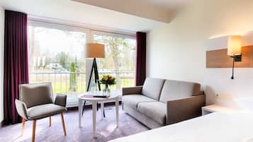 A hotel room with a bed, a sofa, a chair, a small table with a vase of flowers, and a lamp.