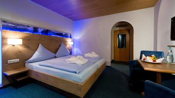 Een hotelkamer met een houten bed, een nachtkastje, een bureau met stoel en een aan de muur bevestigde televisie.