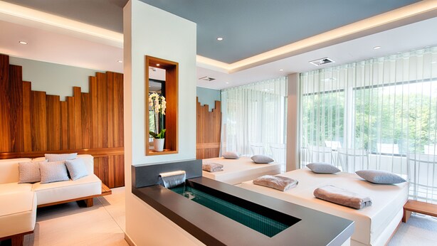 A modern spa room with a large bathtub, a sofa, and a bed with towels. - Seehotel am Stausee (Gerolstein)