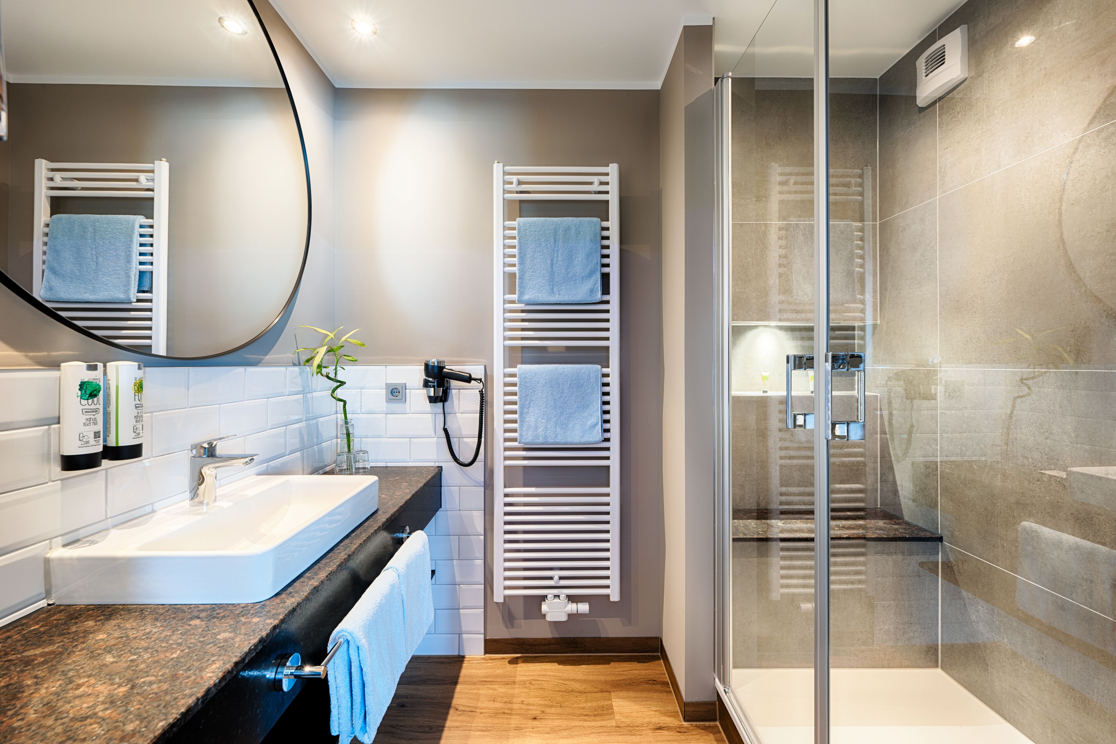 Un baño moderno con cabina de ducha de vidrio, toallero blanco y lavabo con encimera de granito.