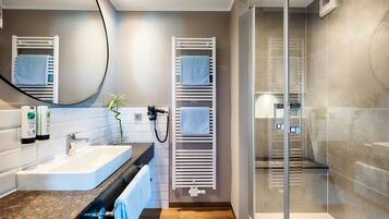 Un baño moderno con cabina de ducha de vidrio, toallero blanco y lavabo con encimera de granito.