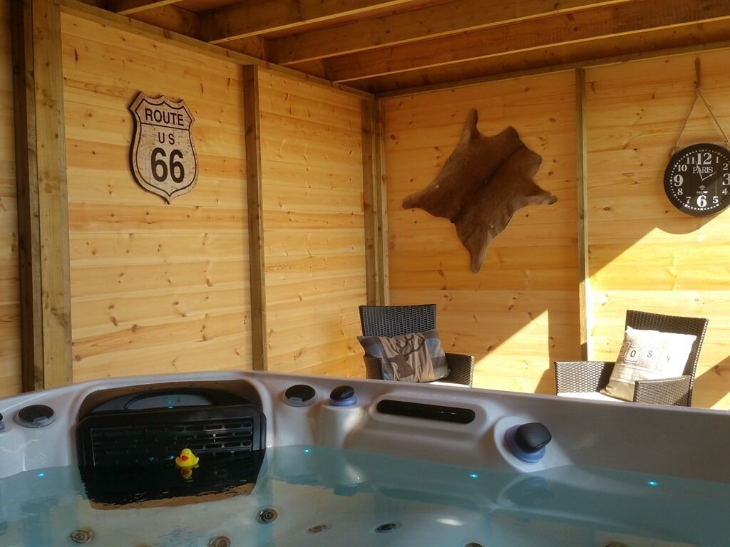 Interior de una cabaña de madera con un jacuzzi, un cartel de la Ruta 66, un reloj y un trofeo de piel de animal montado.