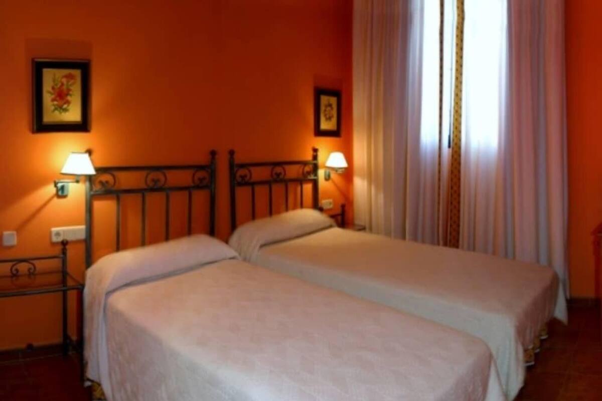 A room with two beds, a metal headboard, two wall-mounted lamps, and a window with curtains.