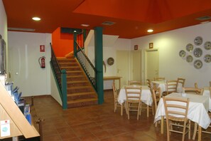 A dining area with tables and chairs, a staircase with green railings, and a fire extinguisher on the wall. - Hotel La Casa Rural (Chinchon)