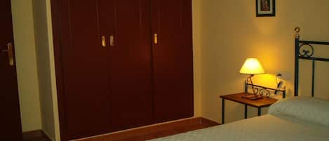 A bedroom with a bed, a nightstand with a lamp, and a wardrobe.