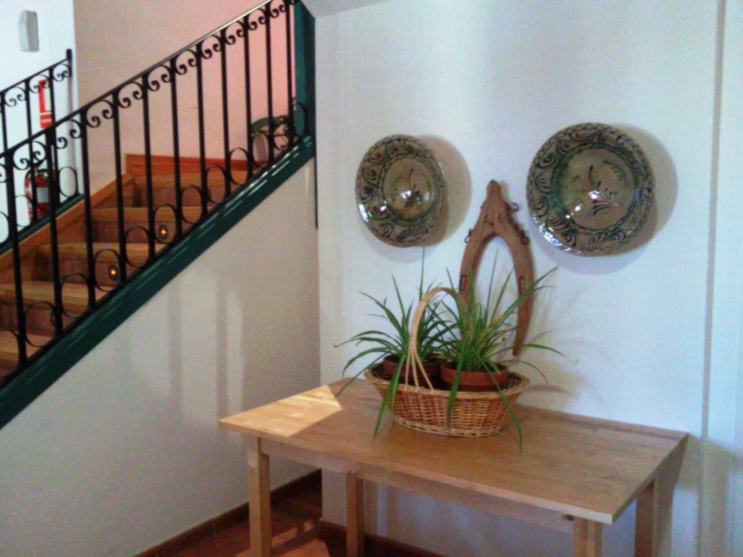 Una escalera con barandilla negra, una mesa de madera con una planta en maceta y platos decorativos en la pared.