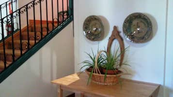 Una escalera con barandilla negra, una mesa de madera con una planta en maceta y platos decorativos en la pared.