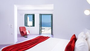 Habitación de hotel moderna con una cama grande, una manta roja y vistas al mar a través de puertas abiertas.