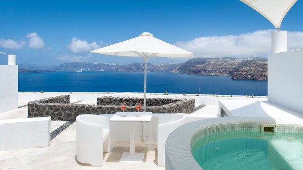 Una zona de estar al aire libre con una mesa, dos sillas, una sombrilla blanca y un jacuzzi.