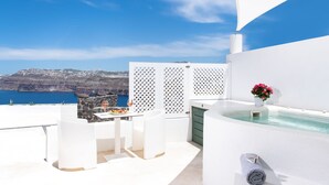 Una terraza exterior blanca con piscina, una mesa con sillas y vistas al mar y a los acantilados.
