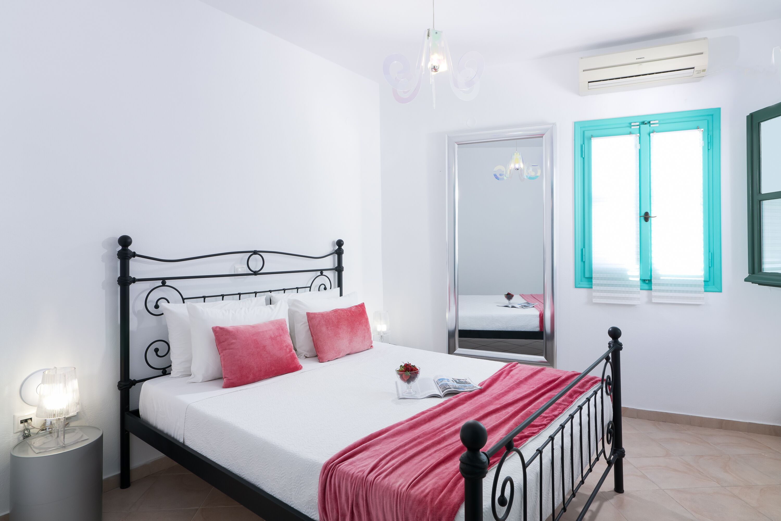 Una cama bien hecha con un edredón rojo, una lámpara de noche y una mesita con lámpara.