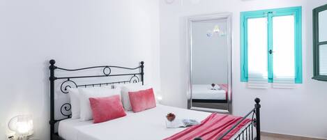 Una cama bien hecha con un edredón rojo, una lámpara de noche y una mesita con lámpara.