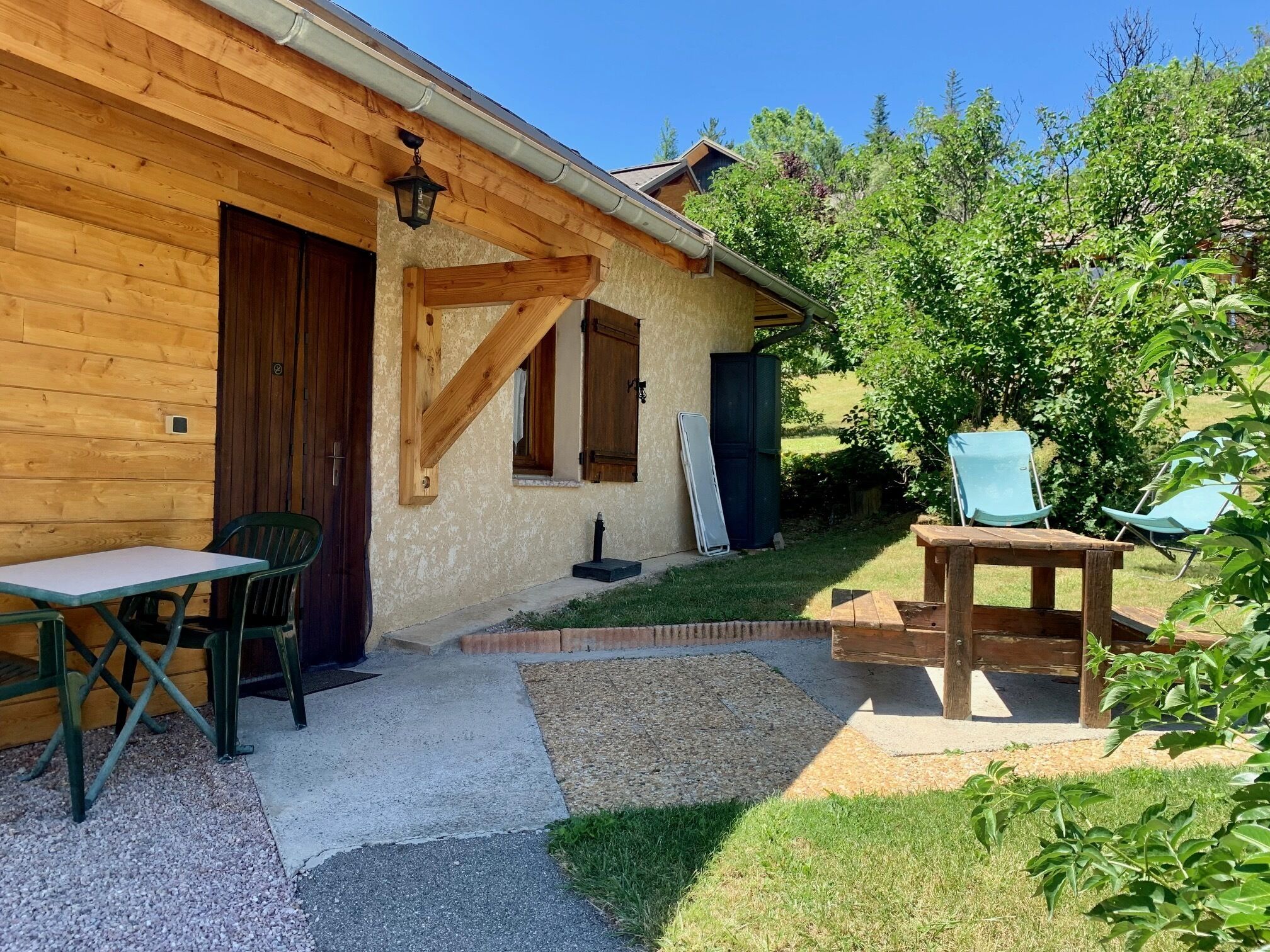 A wooden cabin with a patio area, including a table and chairs, and a small garden with a bench.