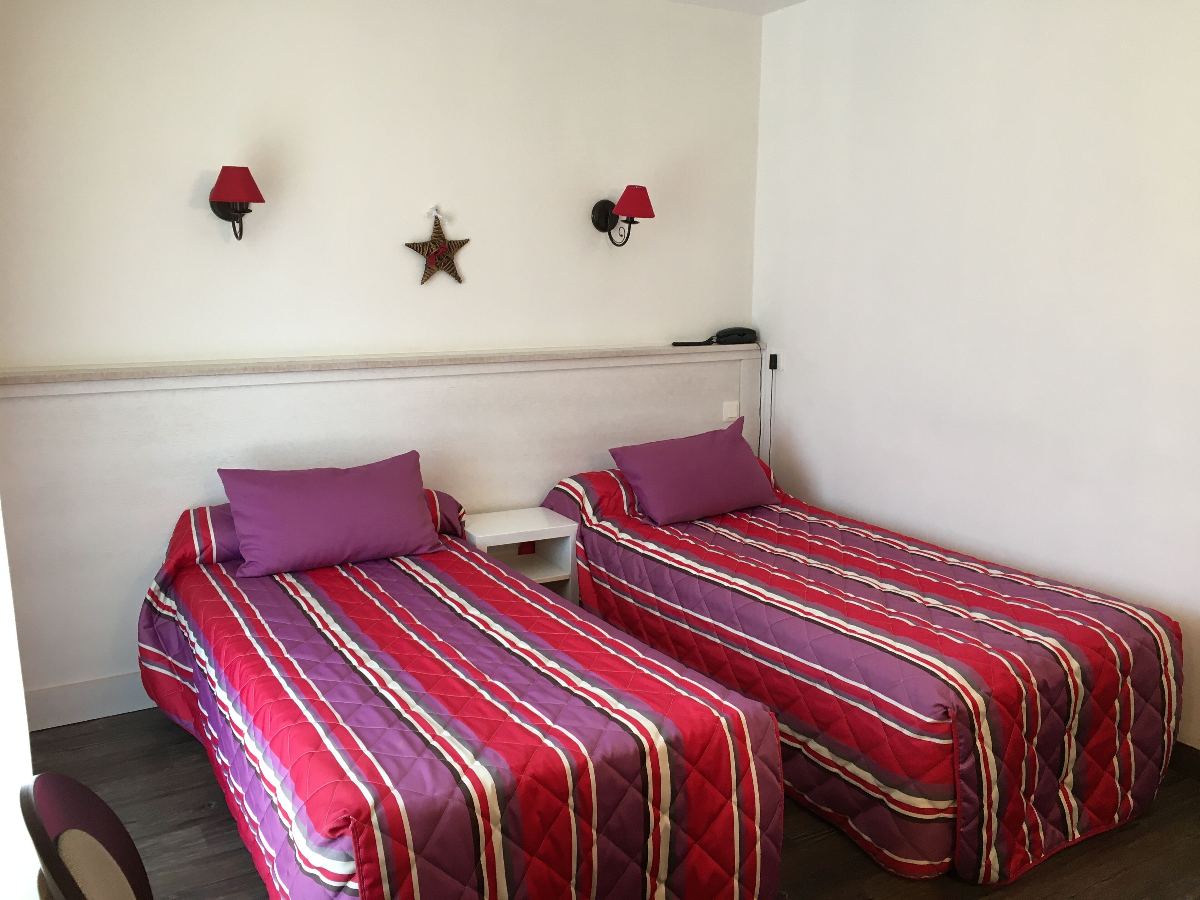 A room with two beds, each with a red and purple striped bedspread, a small white nightstand, and a star decoration on the wall.