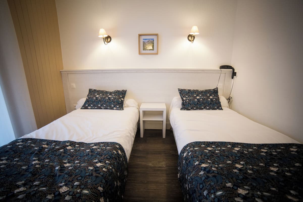 Une chambre double avec deux lits, une petite table de chevet et une lampe fixée au mur.