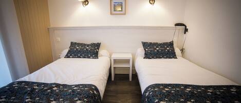 A twin room with two beds, a small bedside table, and a wall-mounted lamp.