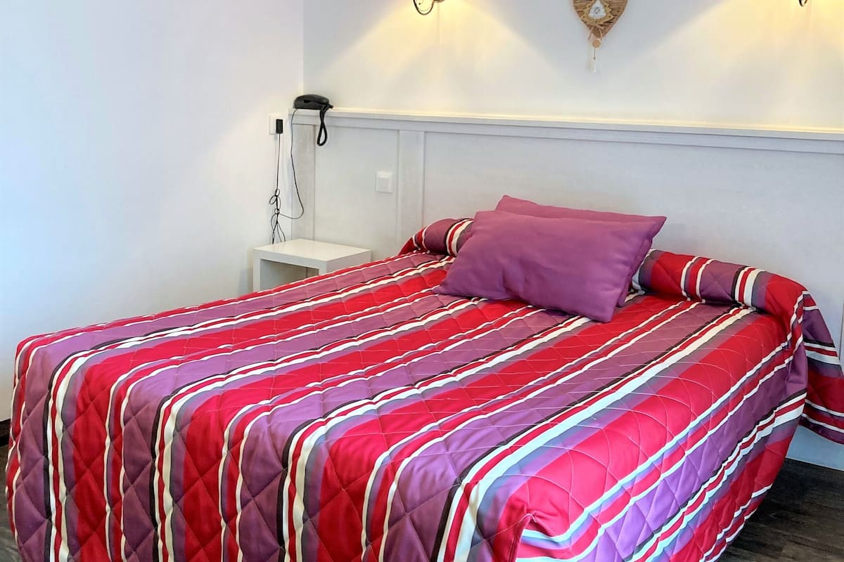 Un lit avec une couvre-lit à rayures rouges et violettes, deux lampes murales rouges et une décoration en forme de cœur accrochée au mur.