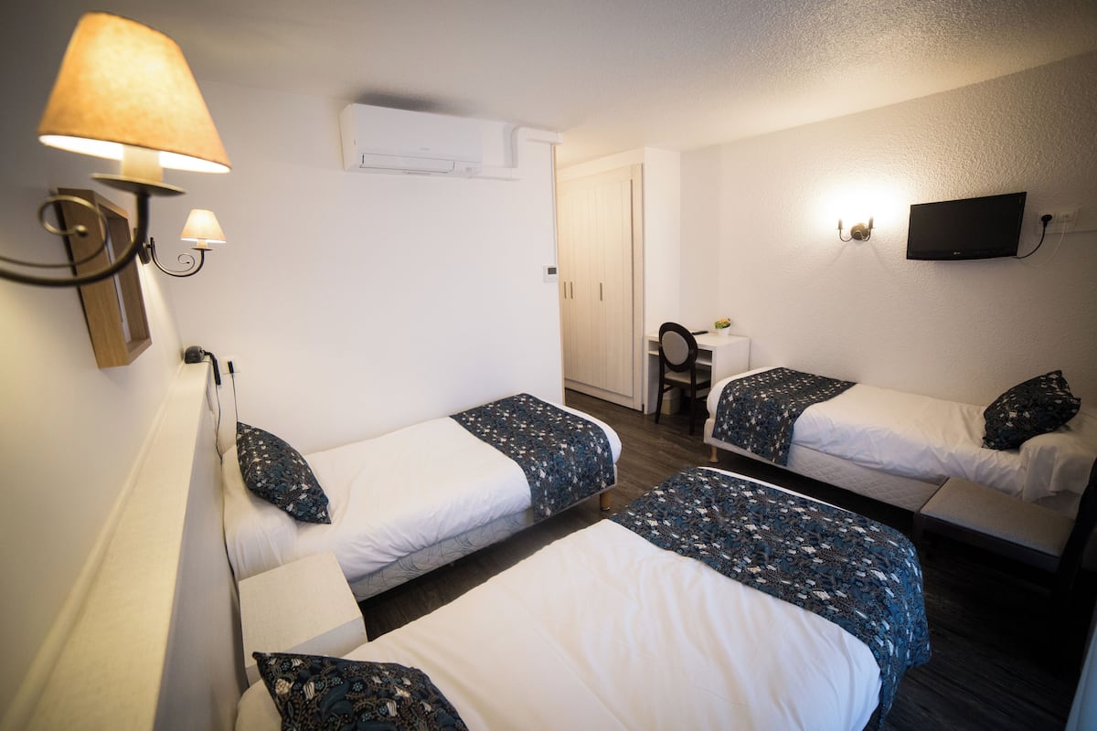 Une chambre d’hôtel avec trois lits, un téléviseur fixé au mur et un bureau avec une chaise.
