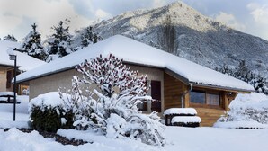 Une cabane en bois, dont le toit est recouvert de neige, avec une chaîne de montagnes en arrière-plan.